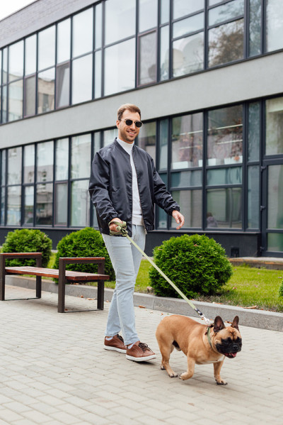 一名微笑的男子牵着法国斗牛犬在城市街道上散步