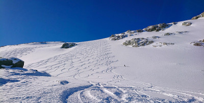 孤身一人的游客从一个满是滑雪和滑雪板痕迹的未经整理的斜坡上滑下。