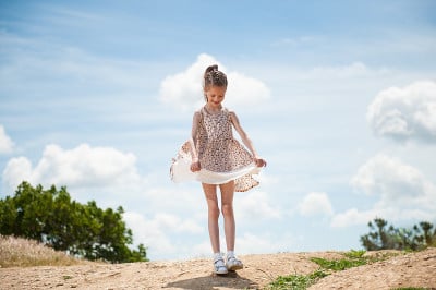 顽皮的小女孩看着她的裙子在风景背景