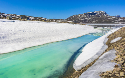 冰冻的绿松石湖瓦瓦滕全景在夏季景观和山脉与雪在挪威海姆塞达尔。