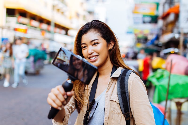 年轻女性游客拿着一个用智能手机拍摄视频的万向节。旅游博客和视频博主的概念