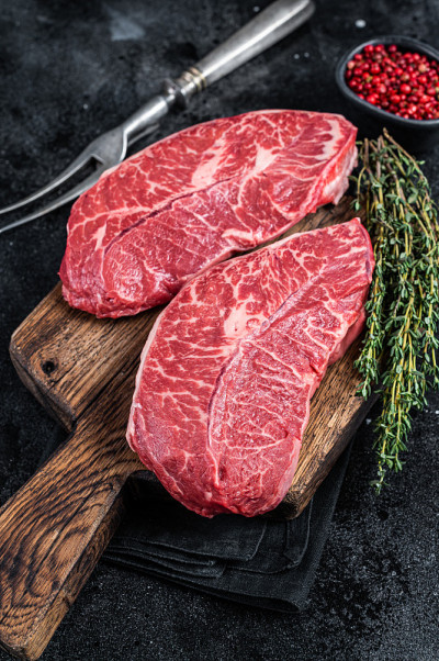 新鲜生的顶部刀片或平铁牛肉排在屠夫砧板上。黑色背景。俯视图