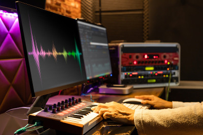 在家庭录音室里，男性音乐制作人用MIDI键盘、电脑和专业设备编曲