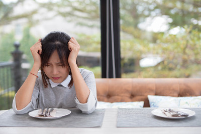 女人独自坐在餐桌上，因为厌食症而感到紧张和头痛