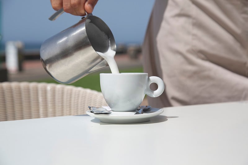 Hand serving milk into coffee cup with blue sky ba