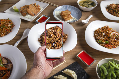 一名男子在东方餐厅用智能手机拍下桌上的食物。