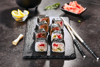 微距拍摄寿司卷在日本餐厅与筷子特写。寿司卷配米饭、炸鲑鱼、飞鱼鱼子酱、黄瓜和辣酱