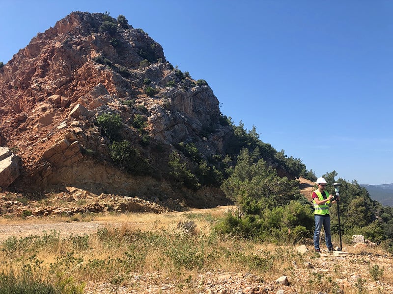 戴着白色安全帽的大地测量工程师在山顶用GNSS卫星接收器进行测量