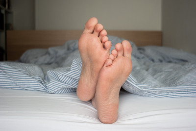 白种人男性脚底交叉从床上的被子中伸出，景深较浅