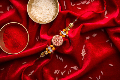 Raksha Bandhan背景以优雅的Rakhi和米粒在红布纹理背景。
