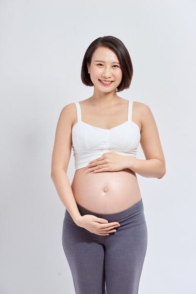 一位美丽的亚洲妇女站在那里抚摸着自己的肚子。怀孕与期望概念