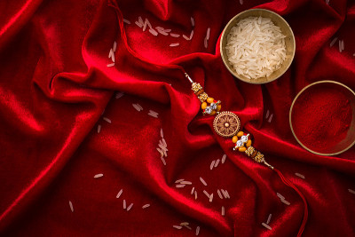 Raksha Bandhan背景以优雅的Rakhi和米粒在红布纹理背景。
