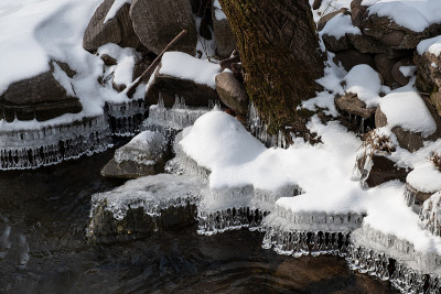 在冬天，惊人的水晶冰柱形状悬挂在白雪覆盖的河岸边缘