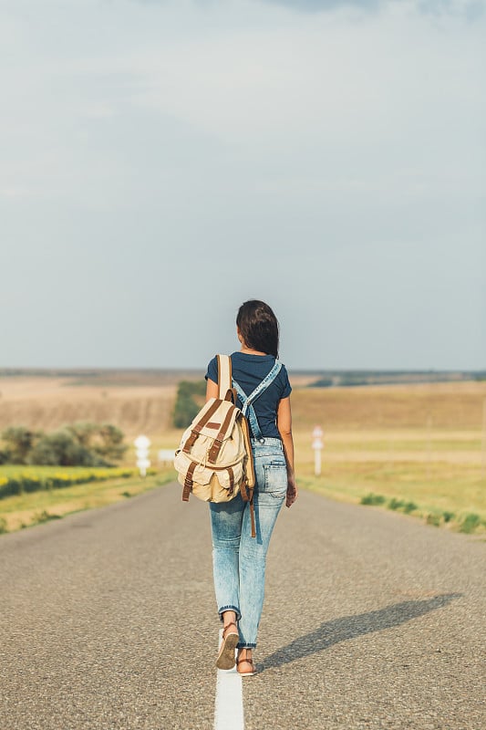 黑发女孩背着背包搭顺风车。concept-travel、冒险、自由。