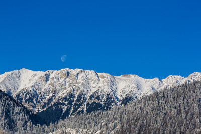 冬天的风景在山上，有白雪覆盖的山峰和落日的月亮