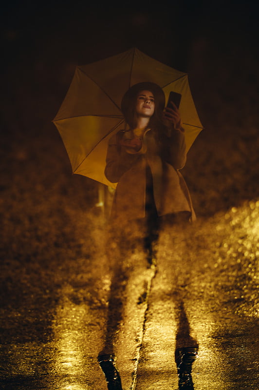 一个女孩拿着黄色雨伞在雨池塘里的倒影