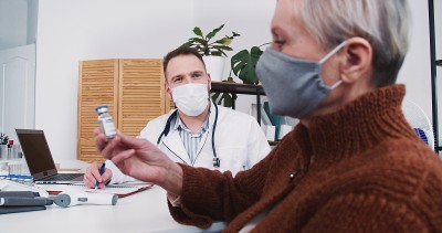 年轻友好的男医生提供疫苗治疗资深病人女子在诊所办公室，护士给他文件。