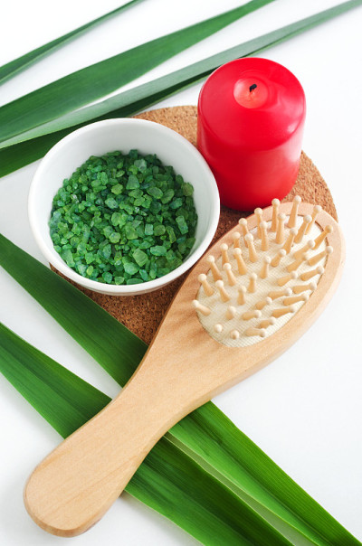 白色的小碗，里面有绿色的浴盐(泡脚)，红色的蜡烛，木制的梳子和绿叶。芳香疗法，水疗和草药概念。