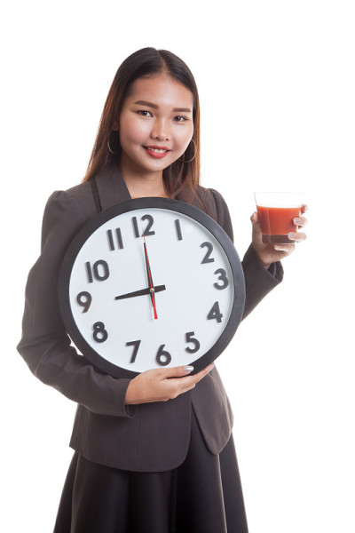 年轻的亚洲女商人拿着番茄汁和钟。