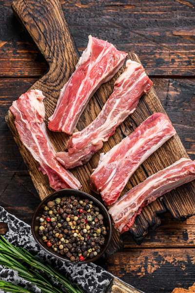 生小牛肉切成薄片，放在木制砧板上。黑色背景。俯视图