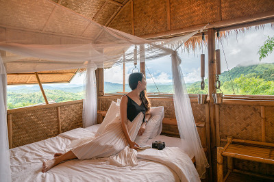 年轻的亚洲女人休息和看着外面的床在木小屋之间的山
