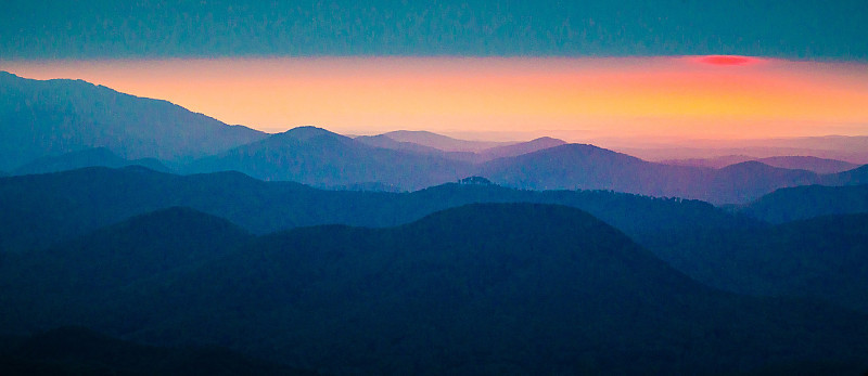 日出的太阳透过云层在山脉上窥视