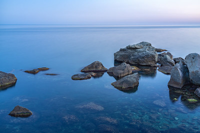 暮色笼罩着荒凉的岩石海滩、海岸线和大海。大海和岩石在夜间的广角视野。