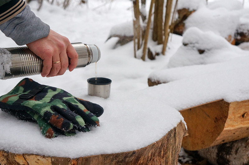 在寒冷的雪地里，将热饮从保温瓶中倒入杯盖