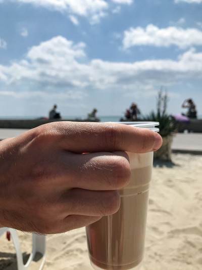 海滩上，一个女人的手拿着装在塑料杯里的卡布奇诺。Balchik。保加利亚。