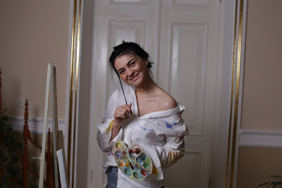 一个漂亮的黑发女孩的工作室肖像，穿着白色衬衫和牛仔裤，画一幅油画。一位微笑着的美丽女子，一位年轻的艺