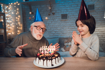 爷爷和孙子晚上在家里。生日聚会。爷爷正在吹生日蛋糕蜡烛。
