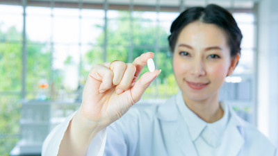 科学家在实验室。妇女研究拿着白色药丸药丸与白色长袍站与脸集中。与背景室内白色实验室。