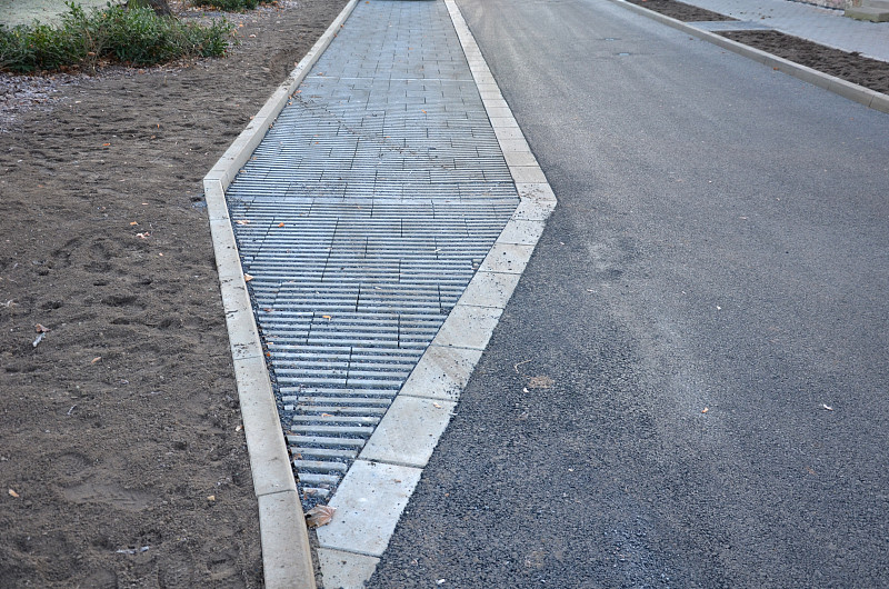 这是城市中新建的一条街道，纵向停车场由灰色混凝土渗透砖和砾石缝隙填充而成。限制水从道路流出的措施