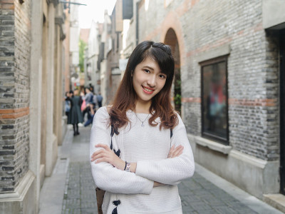 美丽的年轻中国女子身穿白色毛衣和蓝色牛仔裤在上海新天地，微笑的石库门风格街道背景，快乐的时光，亚洲女