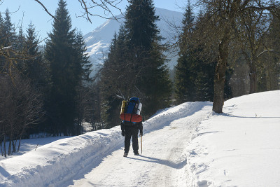 带着冰斧和背包的旅行者在森林里的雪山路上行走