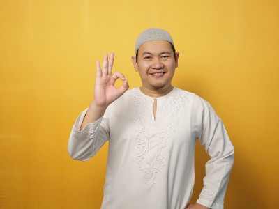 年轻快乐的穆斯林亚洲男子微笑，同时显示OK OK手势，在黄色的背景下