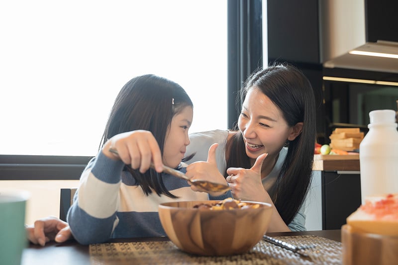 妈妈和女儿在厨房吃牛奶麦片早餐。