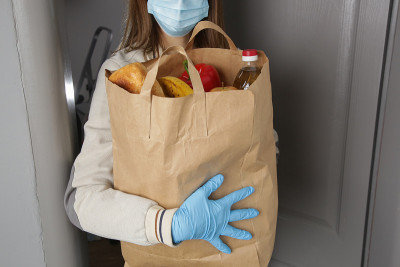 妇女志愿者带着一袋食物和其他必需品给需要帮助的人。送货上门。冠状病毒大流行期间的外卖服务。