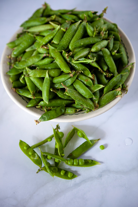 豌豆。白色桌子上的盘子里装着绿色的豌豆荚。收成。健康食品的特写镜头。本空间