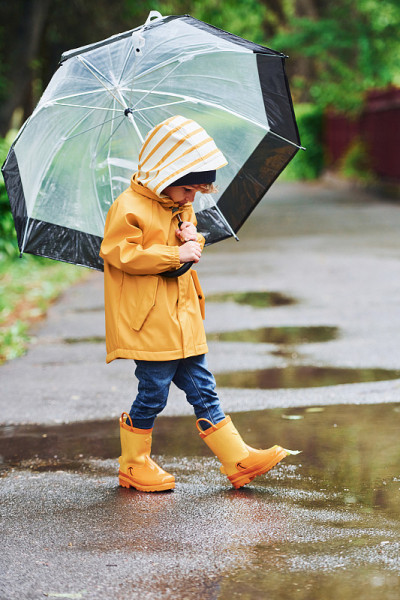 孩子穿着黄色防水斗篷，靴子和雨伞在雨后户外玩耍