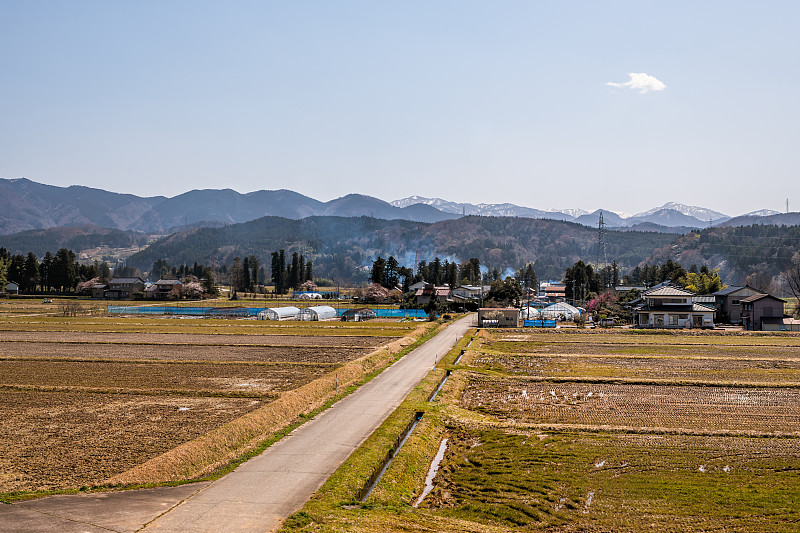 富山，日本岐阜县附近的乡村公路，有传统的农舍和褐色的农田，还有春天从火车上拍摄的山景