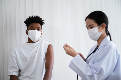女医生或护士正在实验室为等待接种疫苗的非洲裔男子准备冠状病毒19疫苗。预防COVID-19传播的概念
