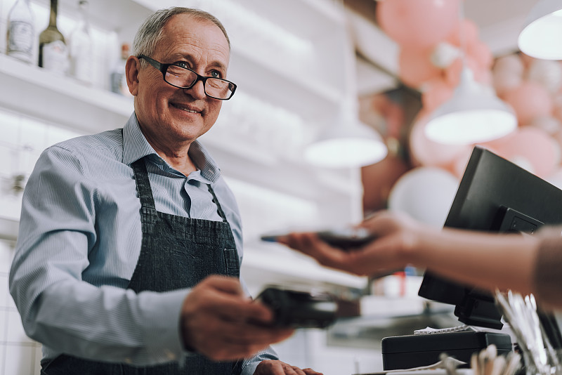 友善的戴眼镜的店主接受顾客的付款