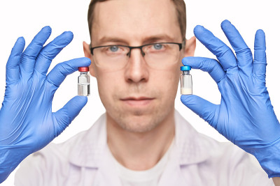 Male person in blue glove hold vaccine bottles. In