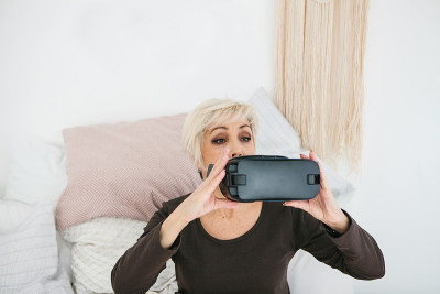 一位上了年纪的妇女准备戴上虚拟现实眼镜，用它来沉浸在虚拟世界中。老一代和新技术。