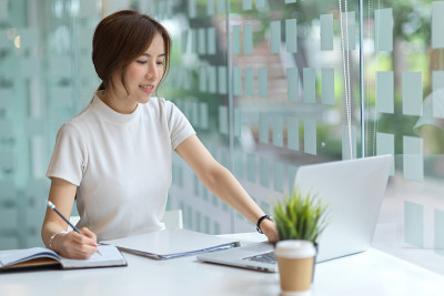 友善的女大学生用笔记本电脑和文具在图书馆做作业