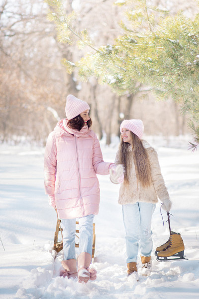 年轻的母亲和女儿在冰雪覆盖的冬天森林里散步