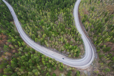 鸟瞰图的蛇形公路。汽车在公路上行驶，穿过春天的森林。