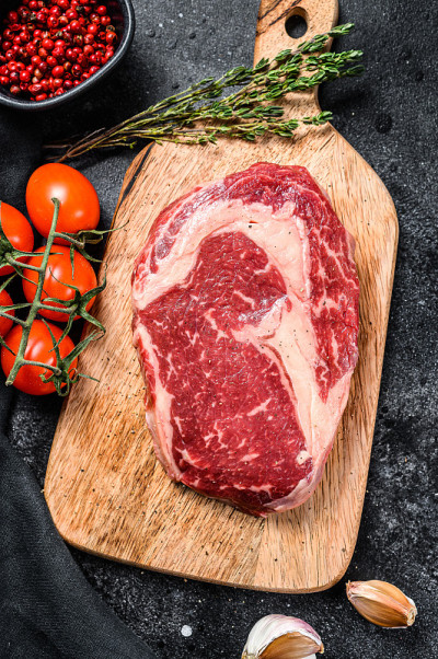 生鲜肉肋眼牛排加调味后放在砧板上。肋眼牛排。黑色背景。俯视图