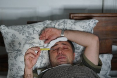 一个又累又病的男人躺在床上检查他的体温
